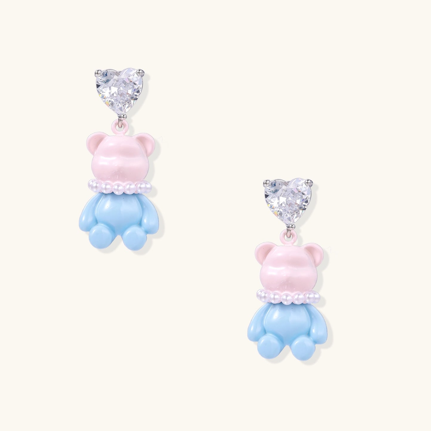 Cute teddy bear earrings with heart-shaped crystals, gold plating, and white pearl accents in pink and blue variants