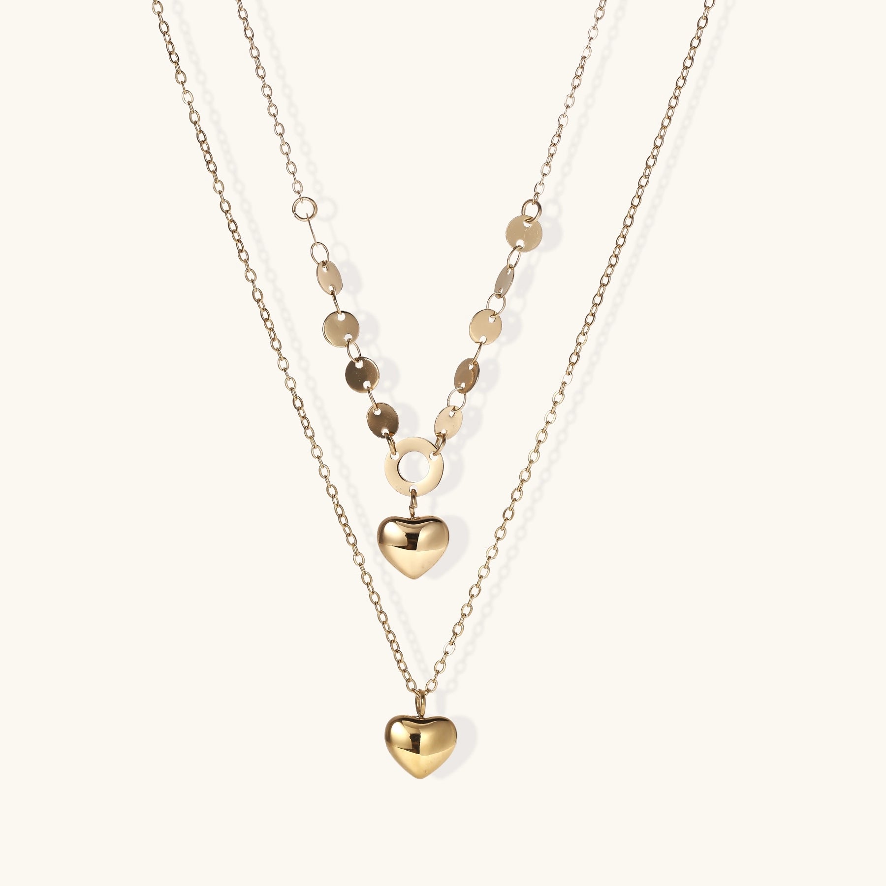 Three-layer gold-plated necklace set with disc chain and two heart pendants on neutral background