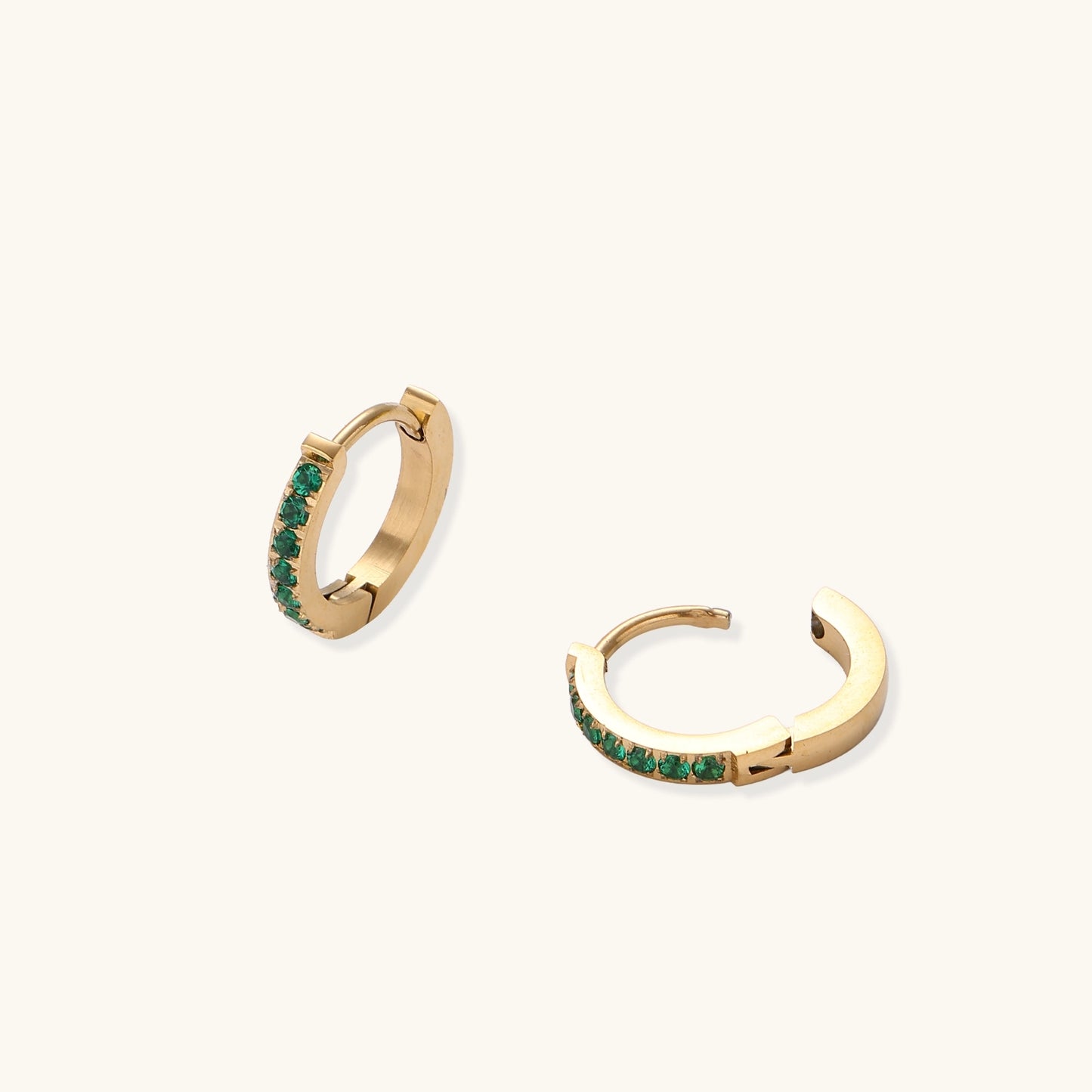 Small gold-plated huggie hoop earrings with emerald green cubic zirconia stones, one open showing hinge mechanism